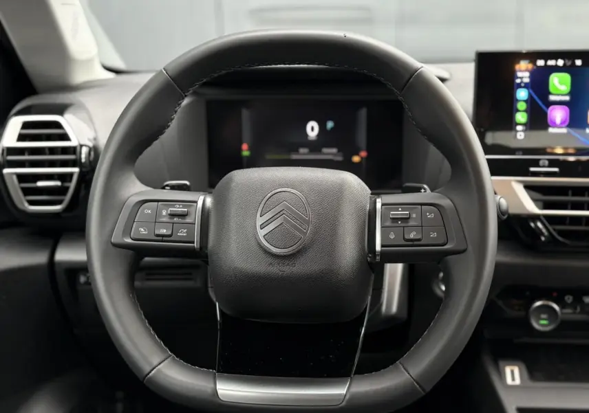 Vue rapprochée du volant cuir noir de la Citroën C4 Hybrid 2025 avec commandes intégrées et tableau de bord numérique.