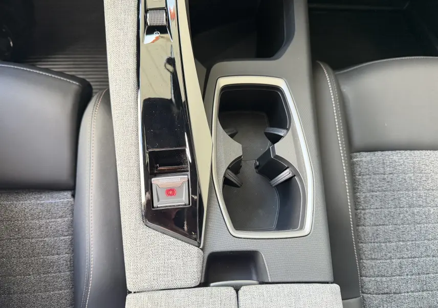 Vue plongeante sur la console centrale grise et noire du Peugeot 1007 Hybrid avec porte-gobelets et bouton frein à main électrique.