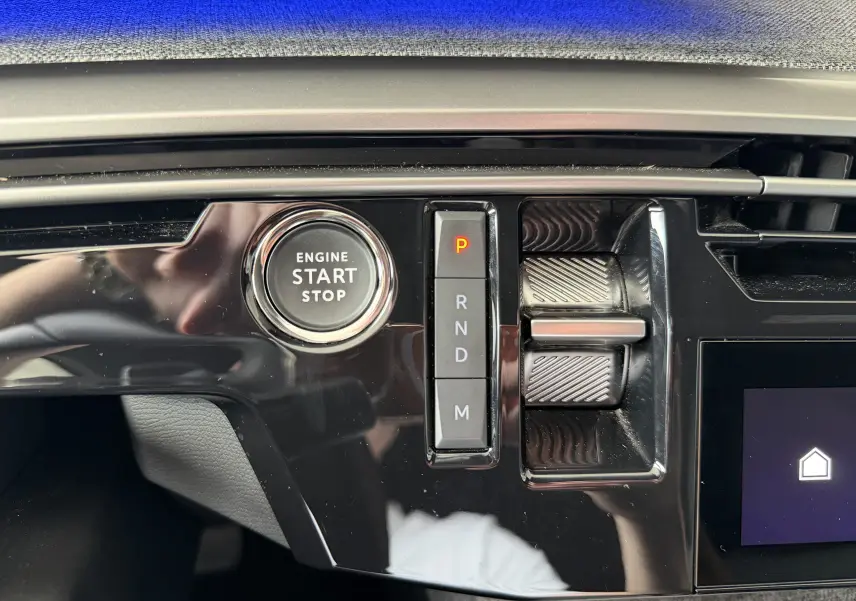 Gros plan sur la console centrale noire brillante du Peugeot 1007 gris, montrant le bouton start/stop et la commande de boîte auto.