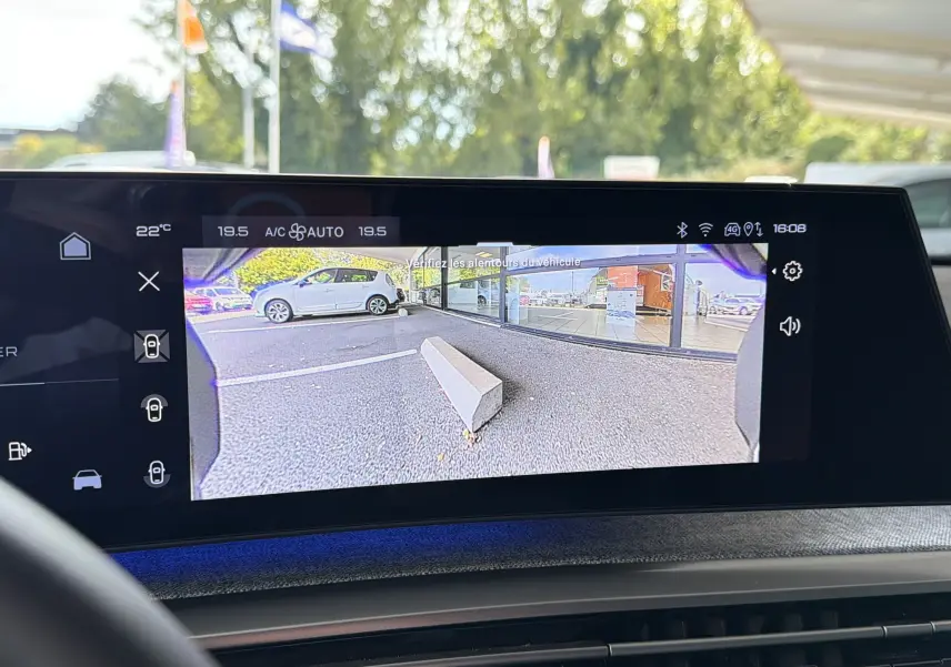 Écran intérieur montrant la caméra de recul d'une Peugeot 1007 gris artense avec vue sur un parking et un trottoir.