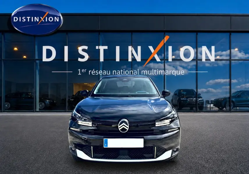 Vue de face d'une Citroën C4 X noire 2025 avec calandre distinctive et phares LED, devant une vitrine Distinxion.