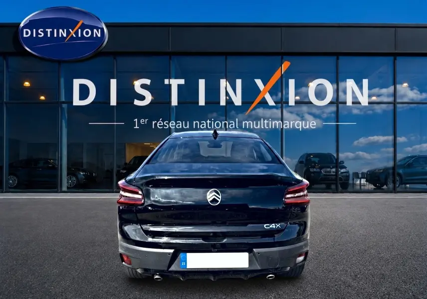 Vue arrière d'une Citroën C4 X noire 2025 avec feux LED et double sortie d'échappement chromée, devant un showroom Distinxion.