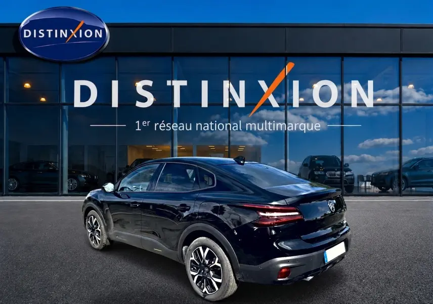 Vue 3/4 arrière droite d'une Citroën C4 X noire 2025 avec feux arrière LED et jantes alu devant un showroom Distinxion.