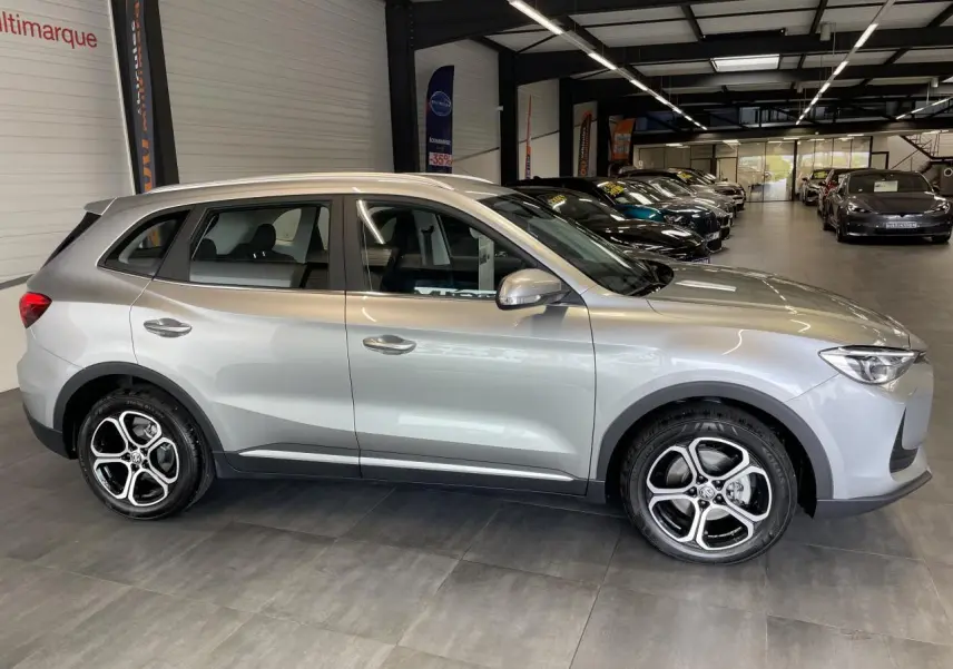 Vue de profil côté gauche du SUV MG ZS 1.5 Hybrid+ gris clair avec jantes alliage 17 pouces en showroom.