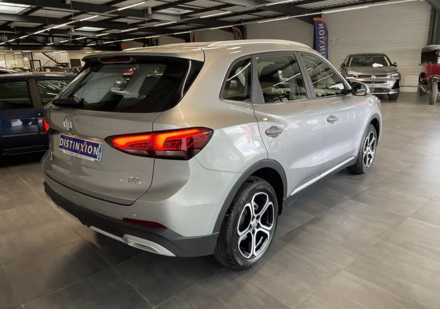 Vue 3/4 arrière droite du MG ZS 1.5 Hybrid+ gris clair avec feux LED allumés en showroom.
