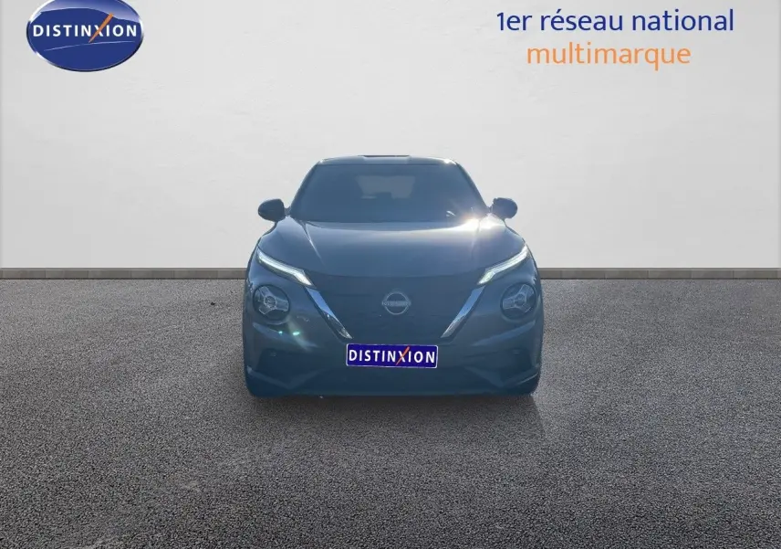 Vue frontale du Nissan Juke 1.6 HEV 143ch gris squale métal avec phares LED allumés sur fond neutre.