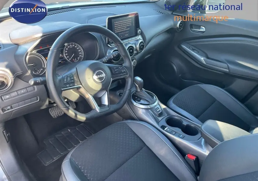 Vue intérieure avant du Nissan Juke 2024 avec volant multifonction, écran tactile et sellerie noire en tissu et cuir.