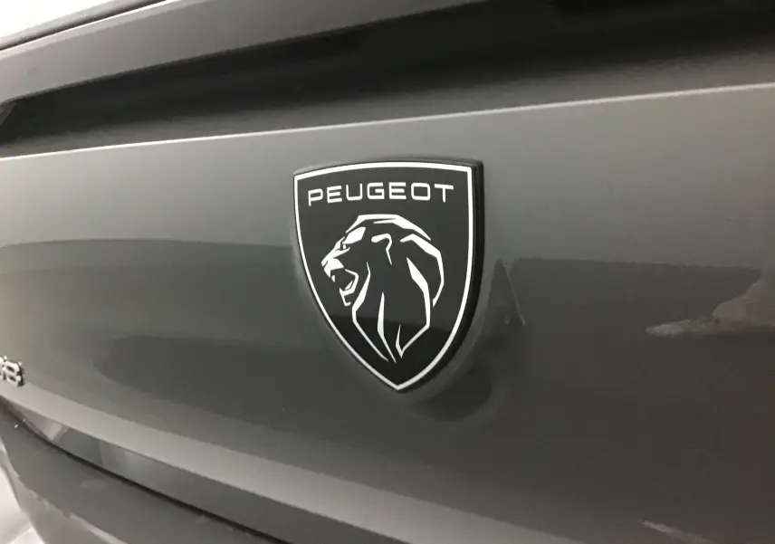 Gros plan sur le logo Peugeot noir et blanc sur la malle arrière d'une 308 gris selenium.