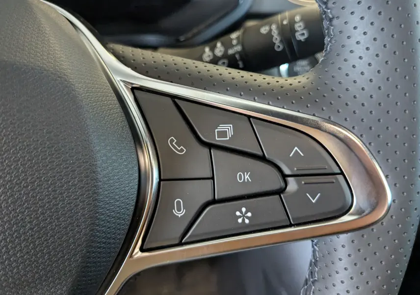 Gros plan sur les commandes multifonctions à droite du volant perforé d'une Renault Captur 2025 hybride.