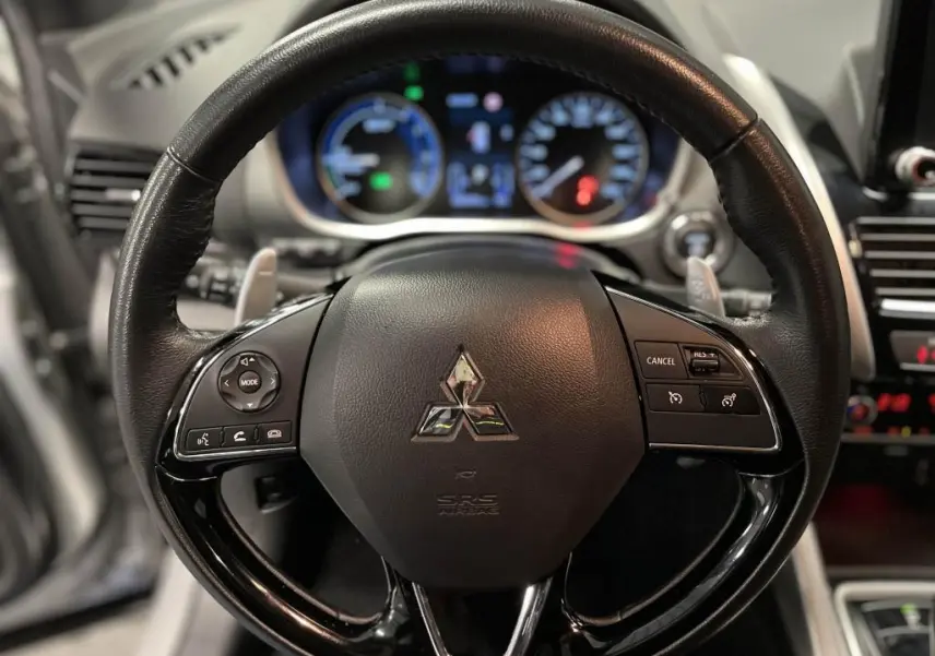 Volant en cuir noir du Mitsubishi Eclipse Cross 2022 avec commandes multifonctions et tableau de bord lumineux en arrière-plan.