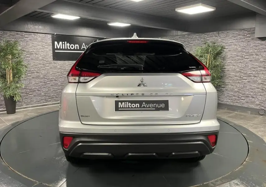 Vue arrière du Mitsubishi Eclipse Cross gris métallisé avec feux arrière LED et logo PHEV visible en intérieur showroom.