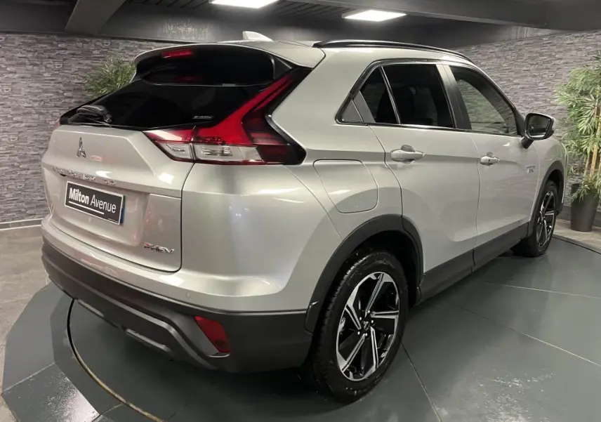Vue 3/4 arrière droite du Mitsubishi Eclipse Cross gris métallisé avec jantes alliage bi-ton et toit noir en intérieur showroom.