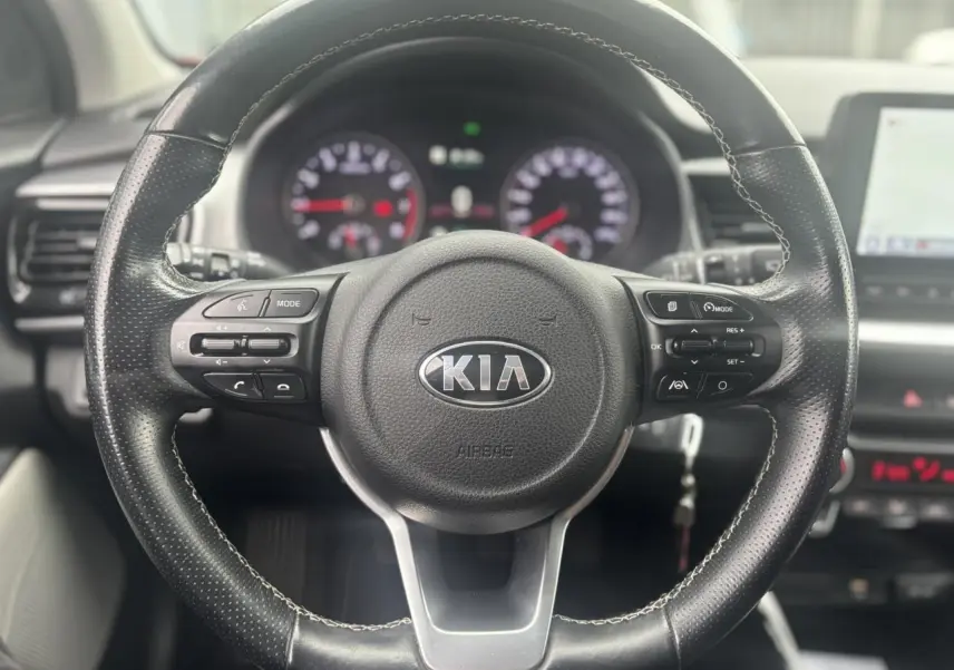 Vue rapprochée du volant noir perforé avec commandes multifonctions du KIA Stonic 2020, tableau de bord flou en arrière-plan.