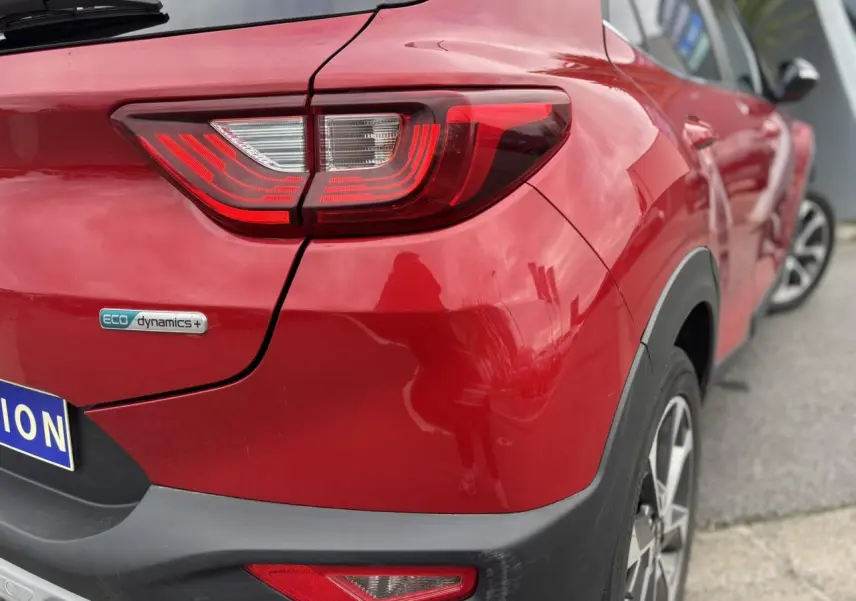 Vue 3/4 arrière droite d'un KIA Stonic rouge métallisé avec feux LED et badge eco dynamics+ visible.