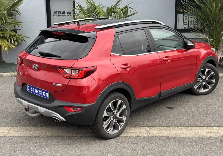 Vue 3/4 arrière droite d'un KIA Stonic rouge métallisé avec attelage et jantes alliage 17 pouces, vitres arrière surteintées.