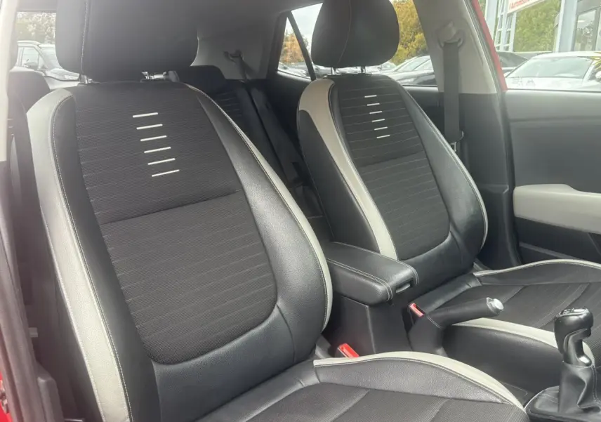 Vue intérieure des sièges avant noirs et gris du KIA Stonic rouge, avec levier de vitesse manuel visible.