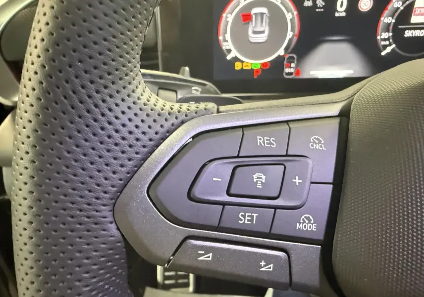 Gros plan sur les commandes de régulateur de vitesse au volant perforé du Volkswagen T-Roc noir intense 2026.