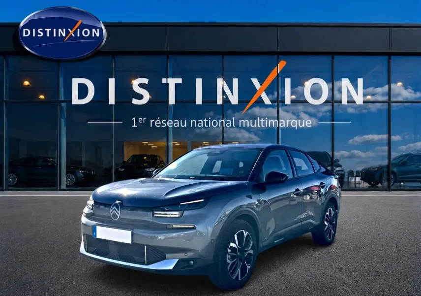Citroën C4 X gris mercure en 3/4 avant droit, avec calandre épurée et jantes alu noires devant showroom Distinxion.