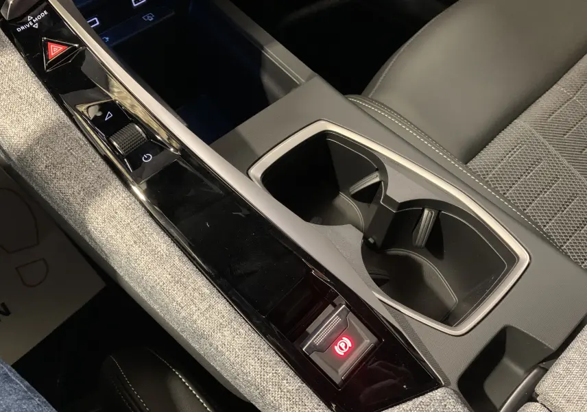 Vue rapprochée de la console centrale du Peugeot 3008 III GT HYBRID 136 e-DSC6 2025 gris Artense, avec commandes et porte-gobelets.