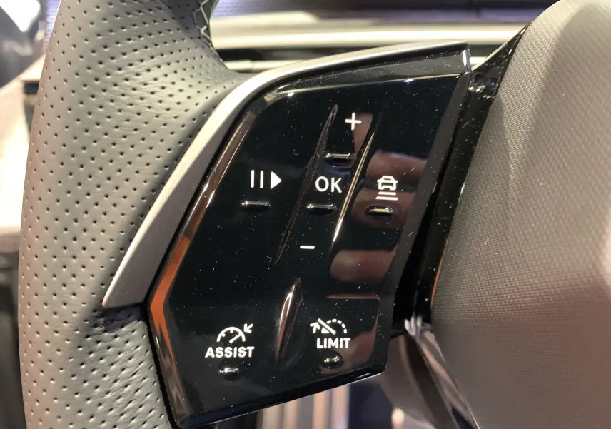 Gros plan sur les commandes noires du volant perforé du Peugeot 3008 III GT Hybrid 136 e-DSC6, côté gauche.