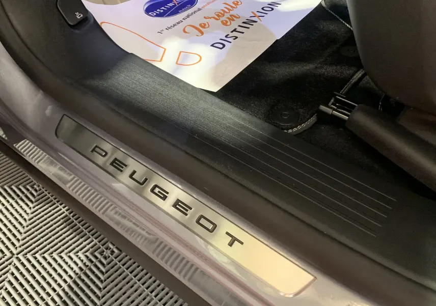 Gros plan sur la plaque de seuil de porte Peugeot à l'intérieur du 3008 gris Artense, côté gauche, avec tapis de sol noir.
