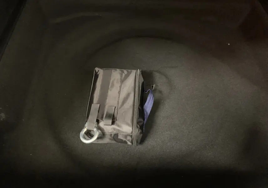 Sacoche noire avec anneau métallique posée dans le coffre du Peugeot 3008 III GT Hybrid 136 e-DSC6 gris Artense, vue intérieure.