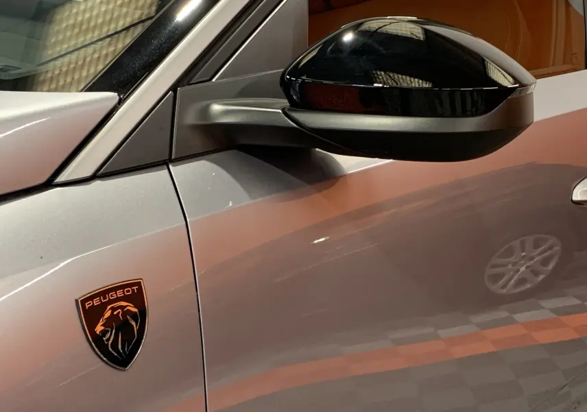 Gros plan sur le rétroviseur noir et l’écusson Peugeot sur la porte gris Artense du 3008 III GT Hybrid 2025 côté gauche.
