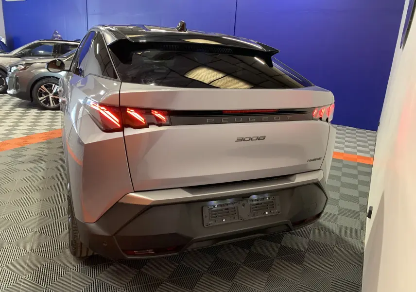 Vue arrière droite du Peugeot 3008 III GT Hybrid 136 e-DSC6 gris Artense avec feux LED allumés en intérieur showroom.