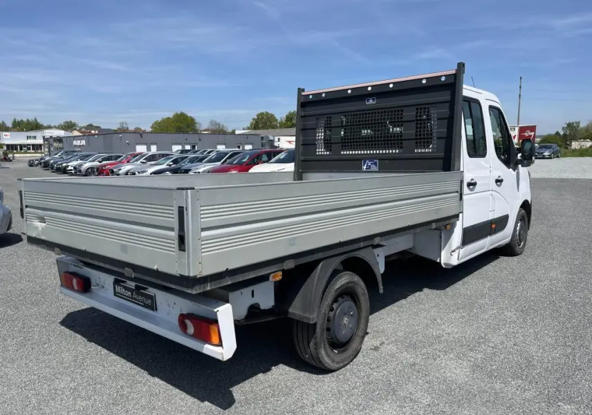 Renault Master blanc en vue 3/4 arrière droit, plateau ridelles aluminium et cabine double visible sur parking.