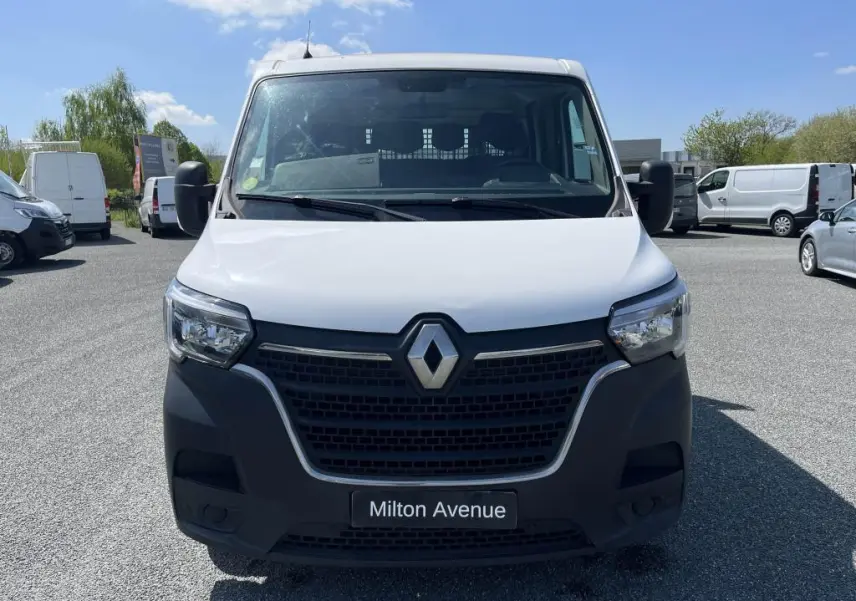 Vue frontale d'un Renault Master blanc avec calandre noire et logo chromé, sur parking ensoleillé.