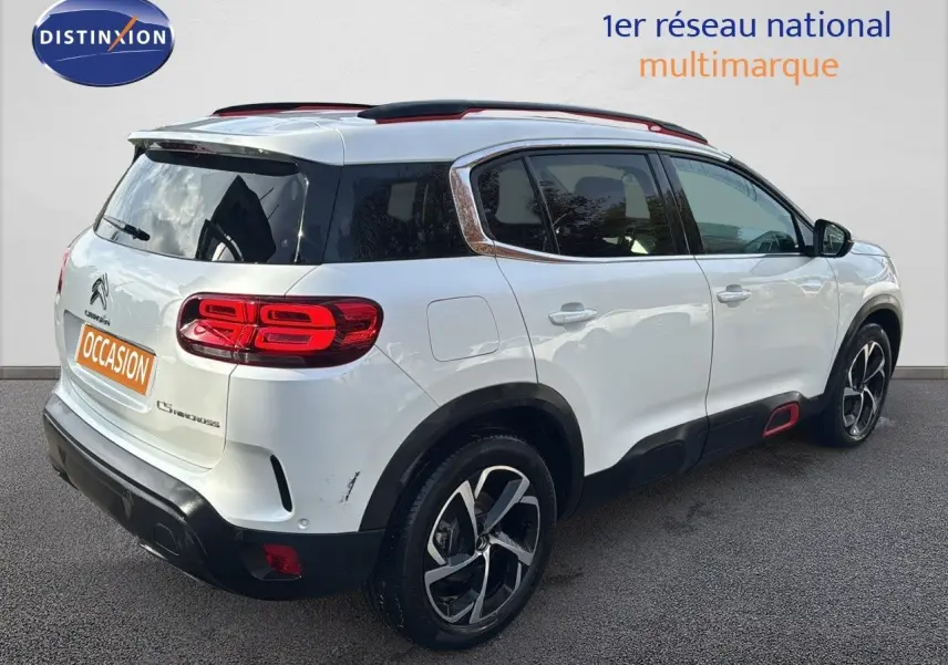 Citroën C5 Aircross blanc nacré vue 3/4 arrière droit, avec jantes noires et détails rouges sur les bas de caisse.