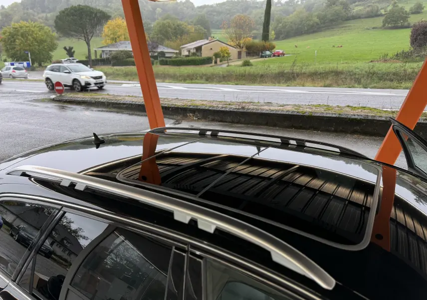 Vue rapprochée du toit ouvrant panoramique et des barres de toit argentées d’une Audi A6 Avant Allroad noire.