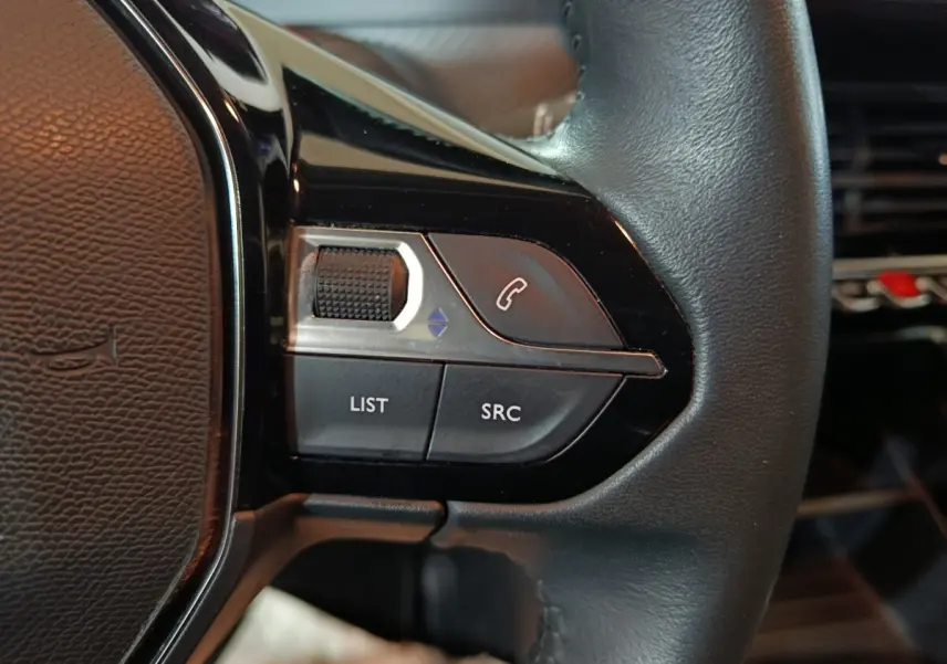 Gros plan sur les commandes gauche du volant noir de la Peugeot 208 1.2 PT 75 S&S Premium, boutons appel et liste.