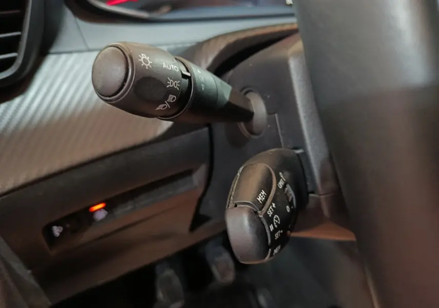 Gros plan sur les commandes de phares et régulateur de vitesse du tableau de bord noir du Peugeot 208 2022.