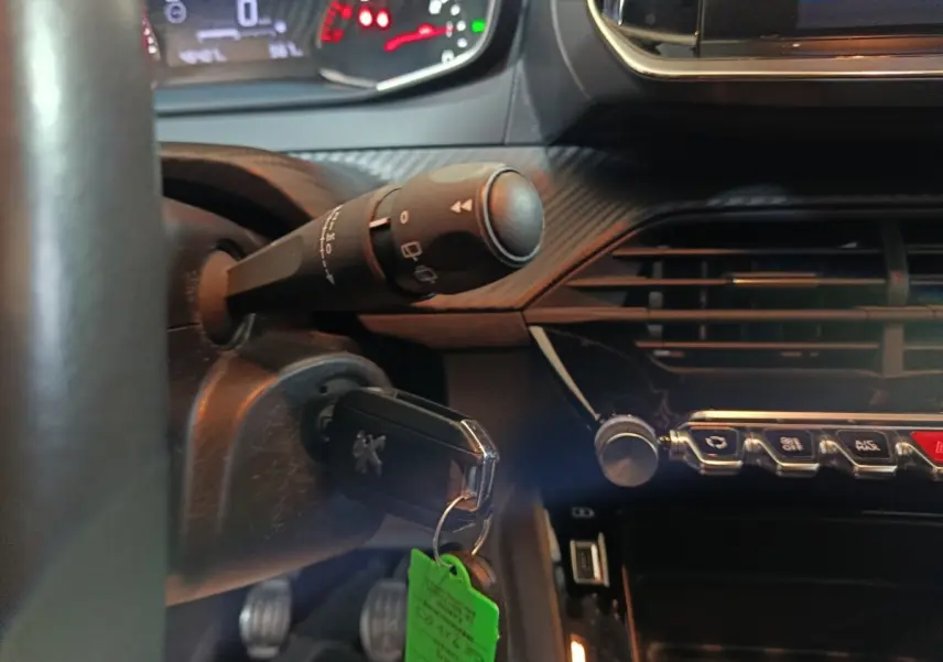 Vue intérieure du tableau de bord noir d'une Peugeot 208 2022, avec clé insérée et commandes centrales visibles.