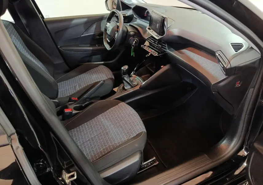 Intérieur avant droit de la Peugeot 208 noire, montrant sièges tissu, volant réglable et écran tactile central.