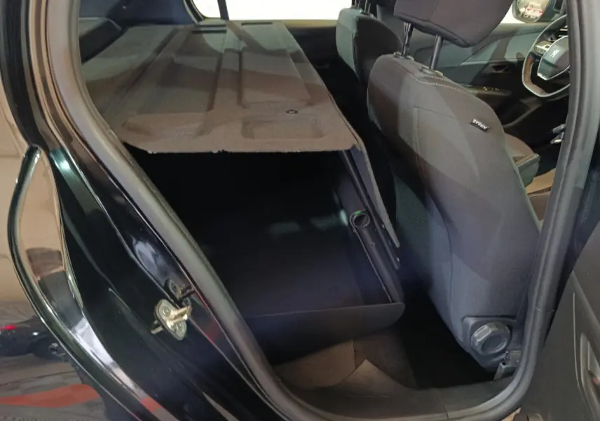 Vue intérieure côté gauche arrière d'une Peugeot 208 noire 2022 avec banquette arrière rabattue et coffre visible.