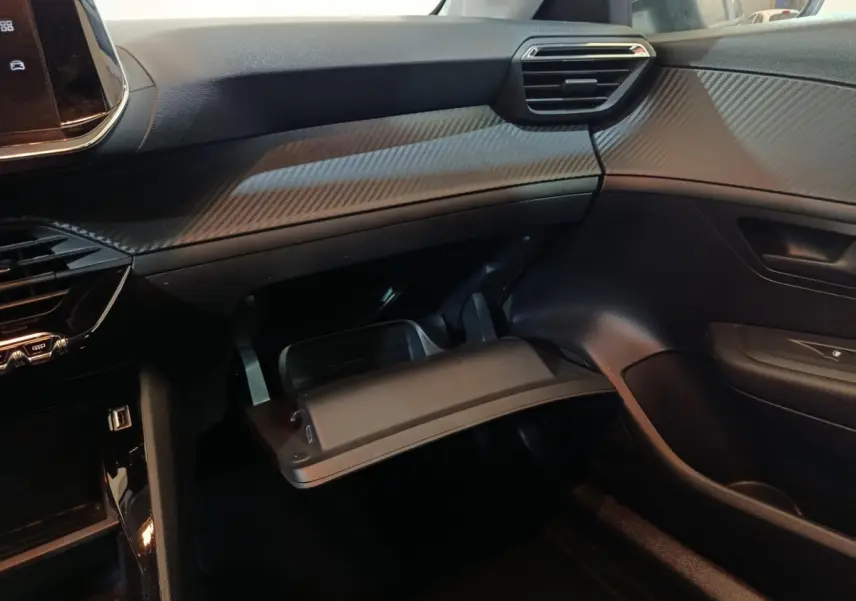 Intérieur côté passager de la Peugeot 208 2022 noire, avec boîte à gants ouverte et tableau de bord texturé.