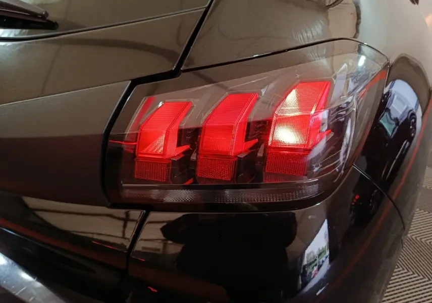 Gros plan sur le feu arrière droit rouge d'une Peugeot 208 noire, mettant en valeur ses trois griffes lumineuses distinctives.