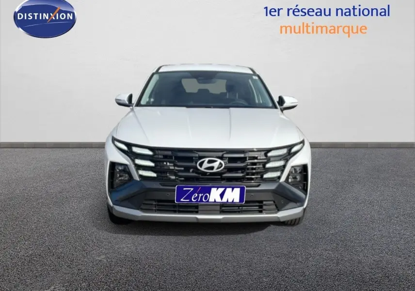 Vue frontale du Hyundai Tucson blanc Atlas 2026 avec calandre noire et feux LED distinctifs allumés.