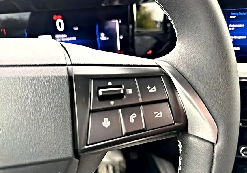 Gros plan sur les commandes multifonctions à gauche du volant gris de l'Opel Mokka 2025, avec écran digital en arrière-plan.