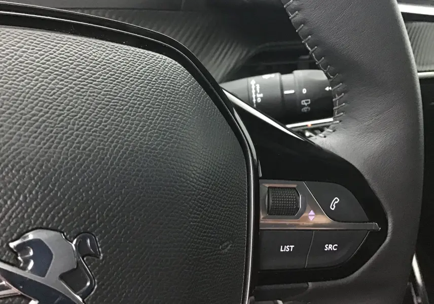 Gros plan sur le volant en cuir noir de la Peugeot 208 Gris Artense, avec commandes audio intégrées à droite.