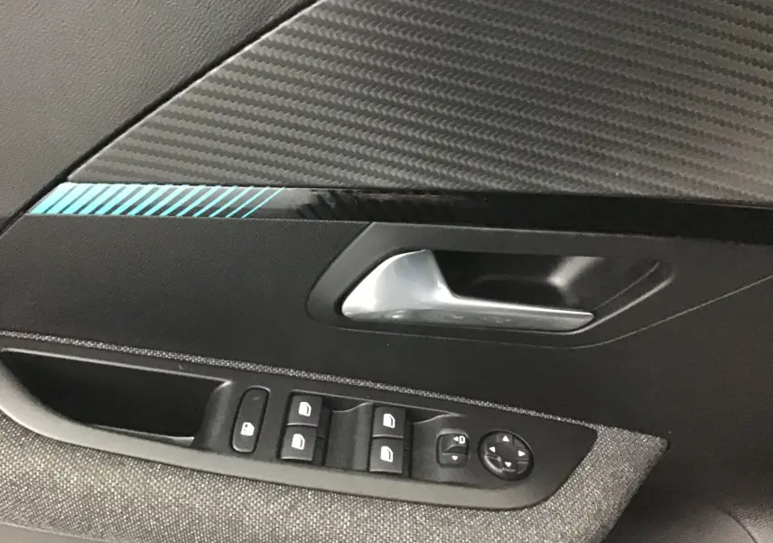 Détail de la porte côté gauche d'une Peugeot 208 gris Artense 2022, avec commandes de vitres et poignée argentée.