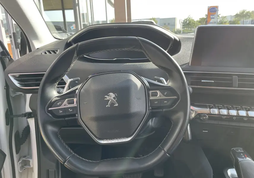Vue rapprochée du volant cuir noir du Peugeot 3008 blanc, avec commandes intégrées et tableau de bord moderne visible.