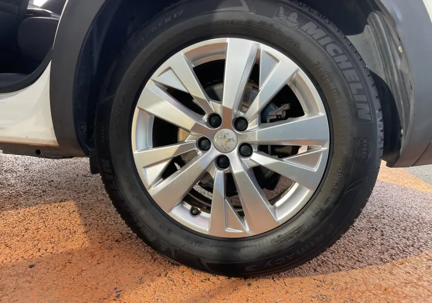 Gros plan sur la roue avant gauche d’un Peugeot 3008 blanc de 2018, jante alliage argentée et pneu Michelin visible.