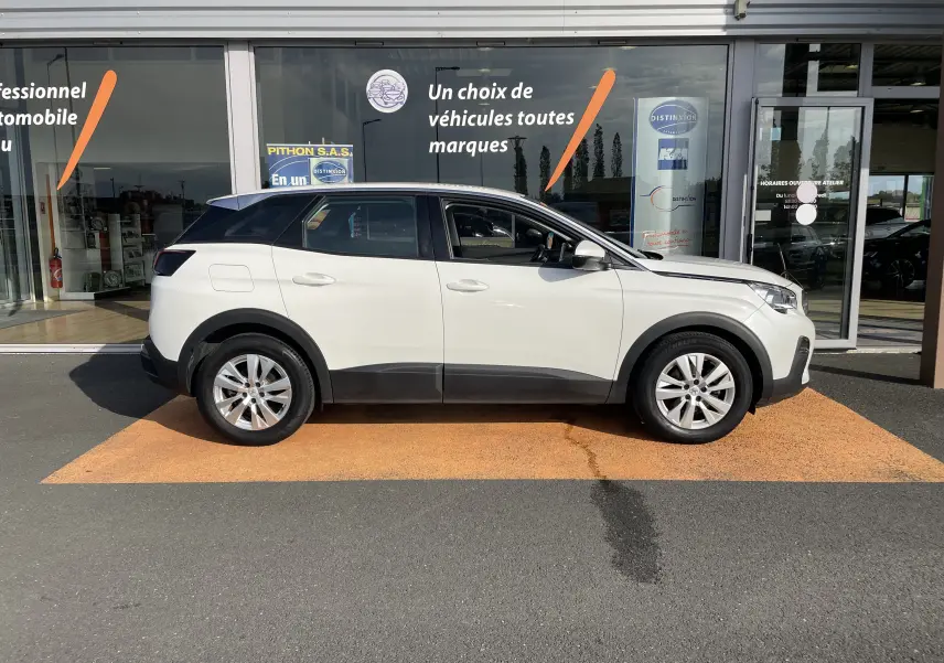 Profil droit d'un Peugeot 3008 blanc de 2018 garé devant une vitrine de concession automobile.