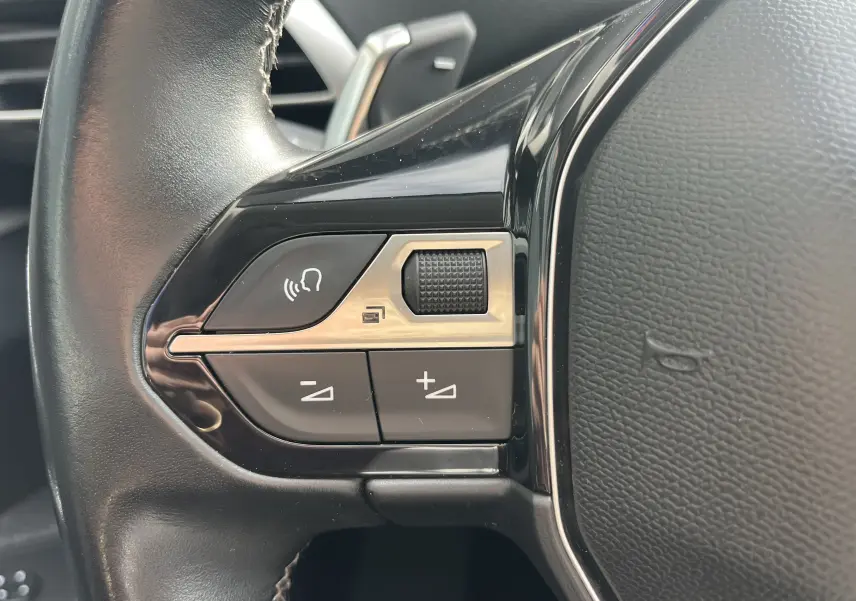 Gros plan sur les commandes gauche du volant noir du Peugeot 3008 blanc, avec boutons de volume et commande vocale.