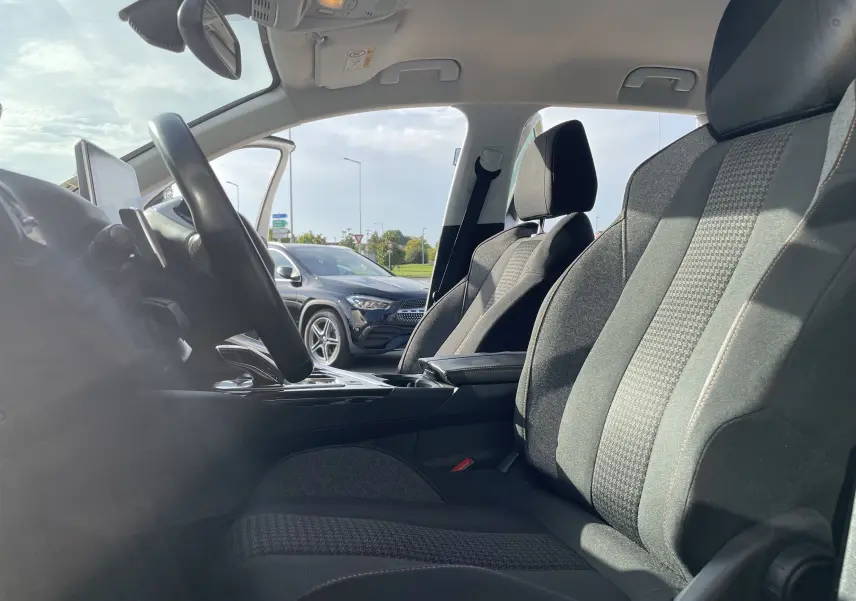 Intérieur avant du Peugeot 3008 2018 avec sièges gris-noir, volant multifonction et porte conducteur ouverte sur fond extérieur.