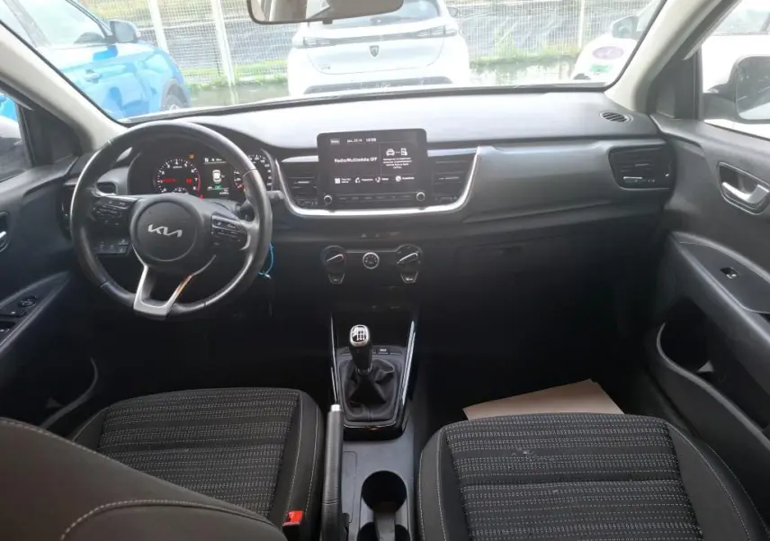 Vue intérieure avant du Kia Stonic blanc 2022, montrant le volant multifonction, écran central et levier de vitesses manuel.
