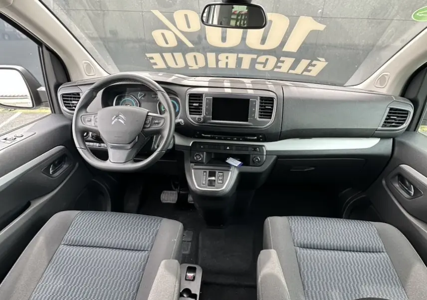 Vue intérieure frontale du Citroën Jumpy van électrique, montrant tableau de bord et sièges tissu noir avec volant multifonction.